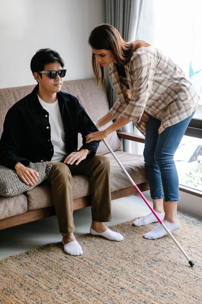 A couple assisting a visually impaired man with a walking stick indoors.