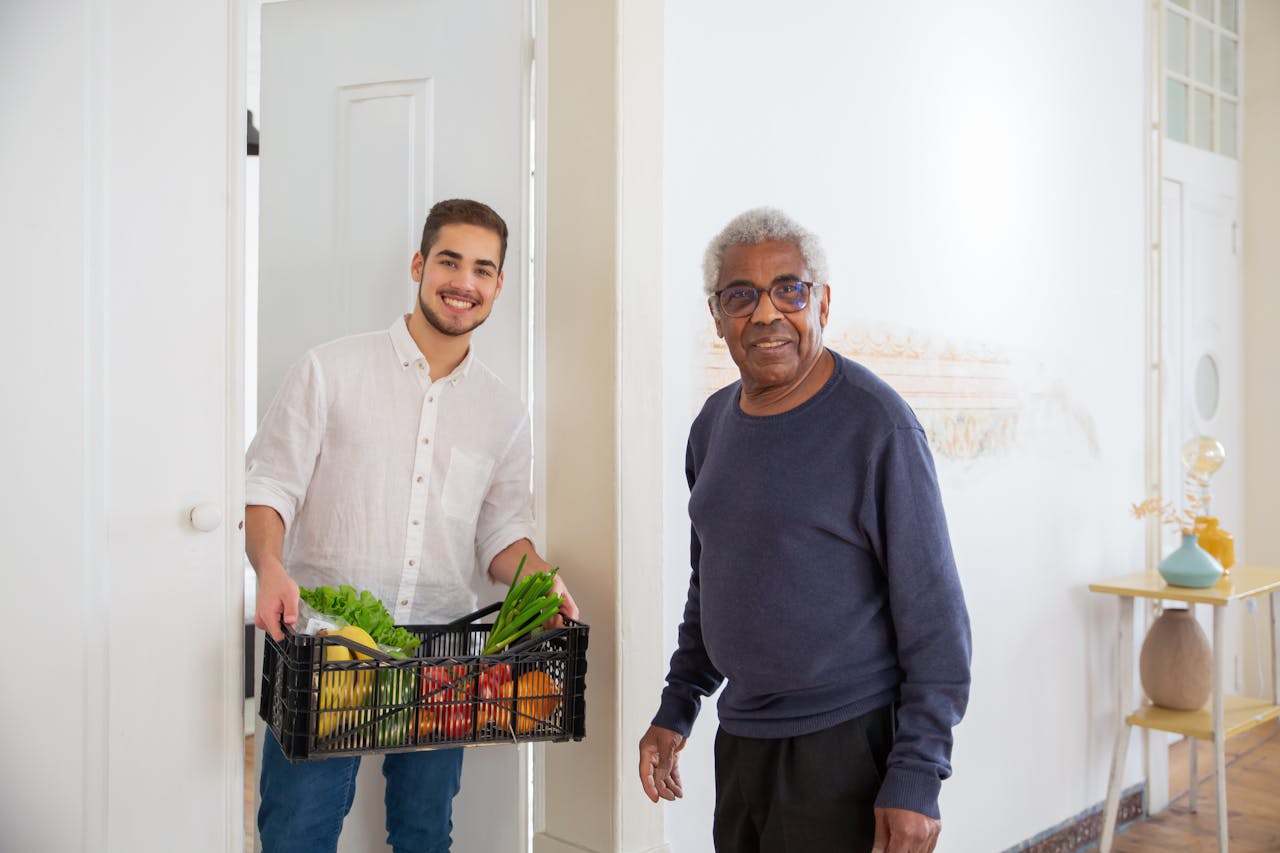 Senior man receiving fresh produce from a young volunteer indoors, promoting community support.