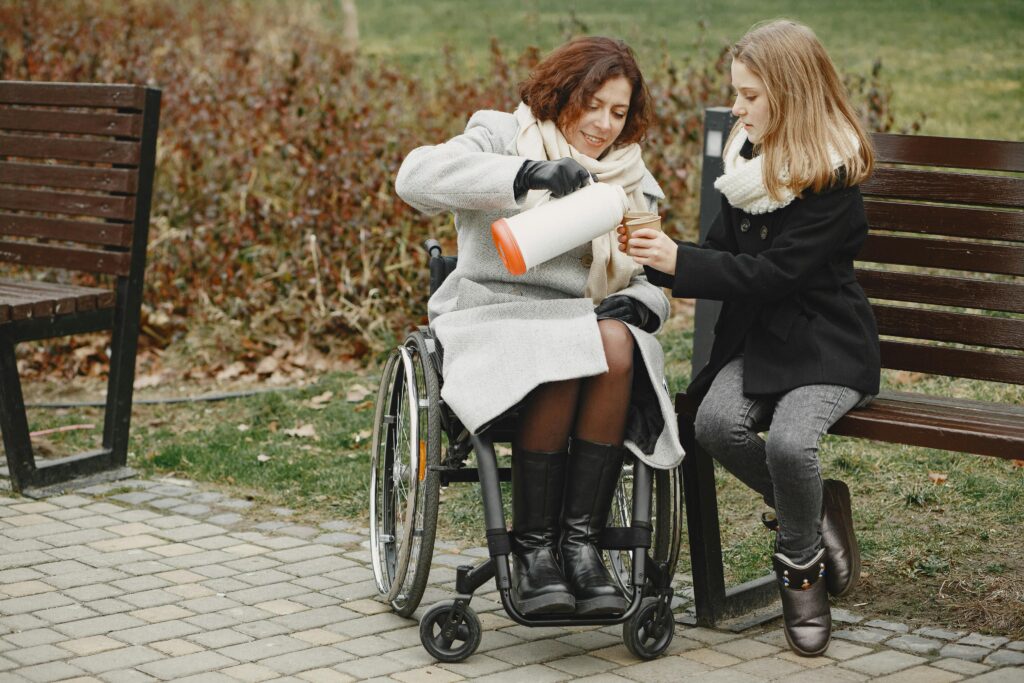 pexels photo 6284848 6284848 A woman in a wheelchair shares a warm drink with a girl in a park.
